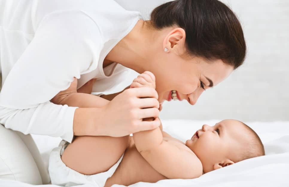 Young woman playing with her cute little baby in bed, when do babies know their name