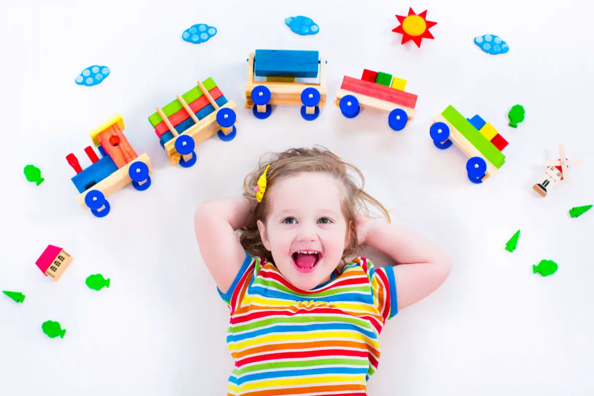 Girl in striped shirt laying on back with toy train above her head. The best Montessori toys for 2 year olds